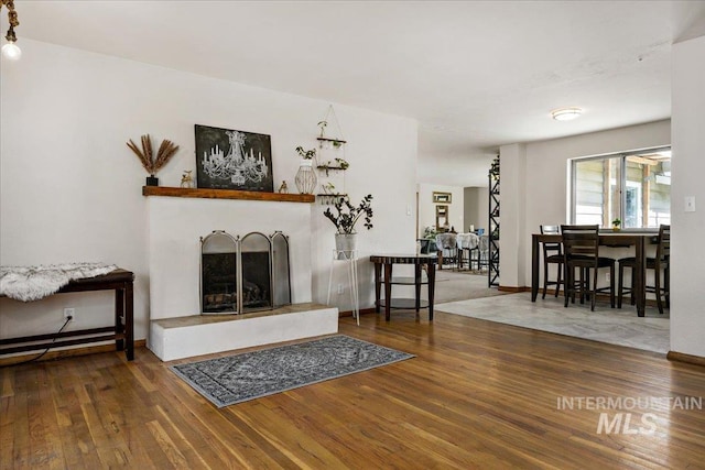 living room with a fireplace with raised hearth, baseboards, and wood finished floors