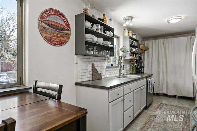 kitchen with a sink, open shelves, dark countertops, tasteful backsplash, and stainless steel dishwasher