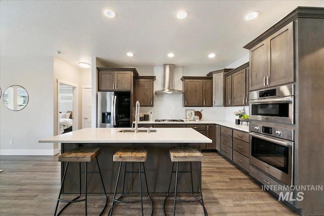 kitchen with stainless steel refrigerator with ice dispenser, a sink, backsplash, wall chimney exhaust hood, and dark brown cabinets