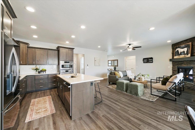 kitchen with a sink, open floor plan, a stone fireplace, stainless steel appliances, and dark wood-style flooring