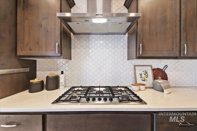 kitchen featuring decorative backsplash, wall chimney exhaust hood, dark brown cabinets, and stainless steel gas cooktop