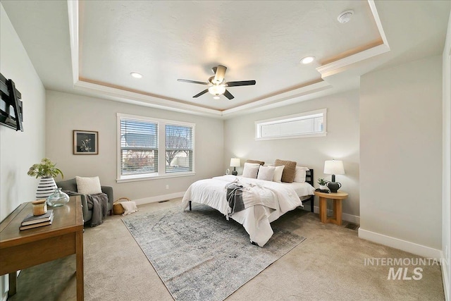 bedroom featuring light colored carpet, baseboards, a tray ceiling, and a ceiling fan