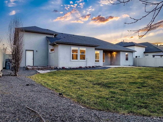 back of property at dusk with stucco siding, a patio, a yard, and fence