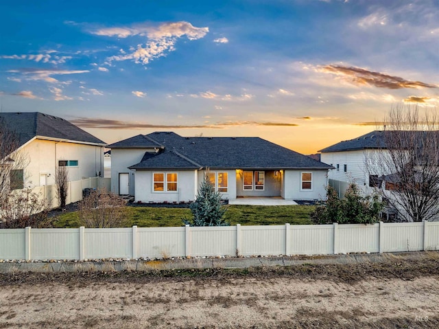 back of property at dusk with a patio area, stucco siding, and a fenced front yard