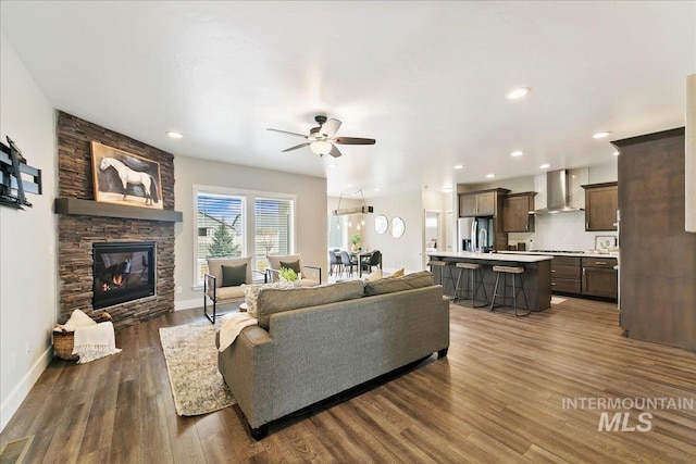 living area featuring baseboards, a stone fireplace, and dark wood-style flooring