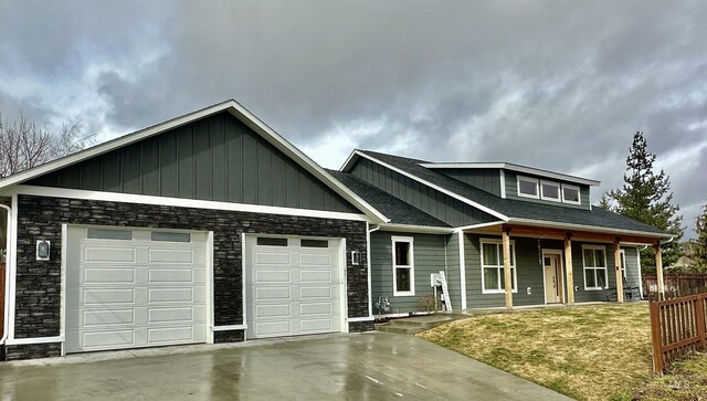 1321 Lande Ln, Moscow, ID 83843 - view of front of home featuring stone siding, fence, covered porch, concrete driveway, and a garage