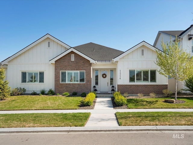 view of front facade featuring a shingled roof, board and batten siding, a front yard, and brick siding