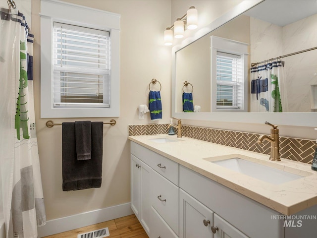 bathroom featuring visible vents, decorative backsplash, a sink, and wood finished floors