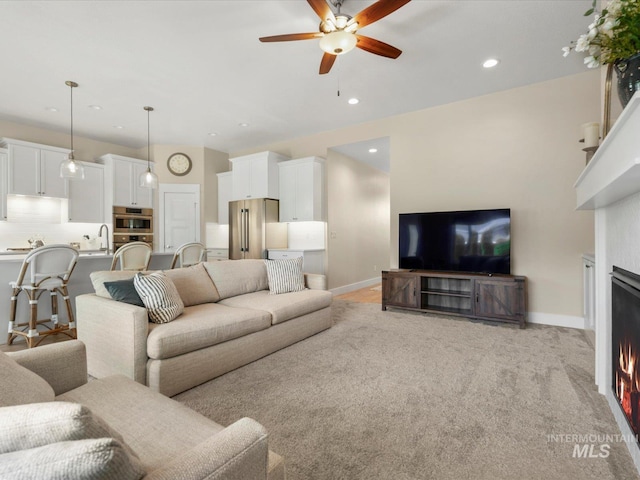 living area featuring recessed lighting, baseboards, ceiling fan, and a warm lit fireplace