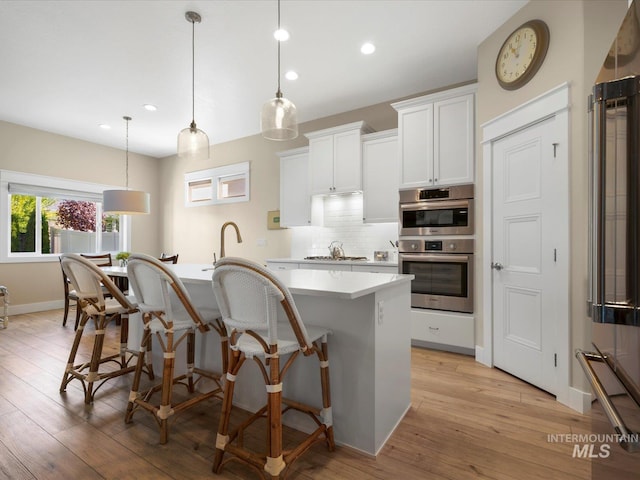 kitchen with a breakfast bar, light wood-style floors, a center island with sink, light countertops, and backsplash
