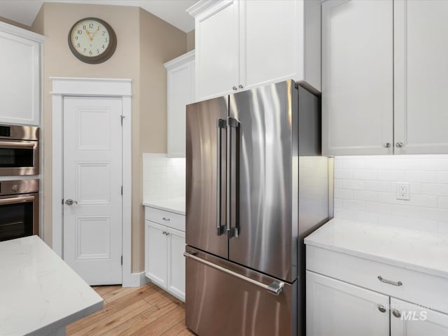 kitchen with stainless steel appliances, white cabinetry, light wood finished floors, and tasteful backsplash