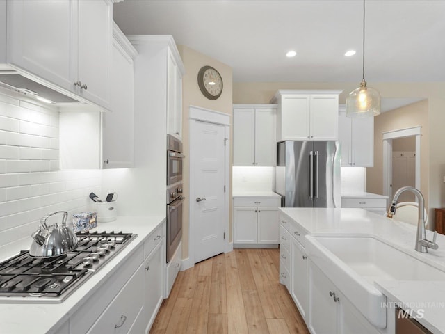 kitchen featuring appliances with stainless steel finishes, tasteful backsplash, a sink, light wood finished floors, and white cabinetry