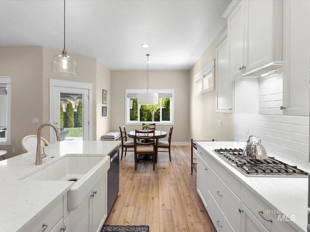 kitchen with a sink, light wood finished floors, stainless steel appliances, white cabinetry, and backsplash