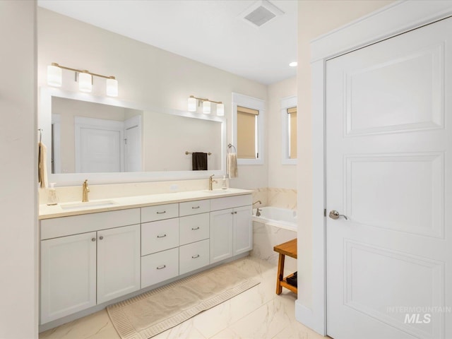 full bath with double vanity, a sink, marble finish floor, and a garden tub