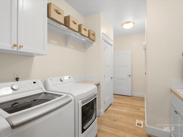 clothes washing area with light wood-style floors, visible vents, cabinet space, and washer and dryer