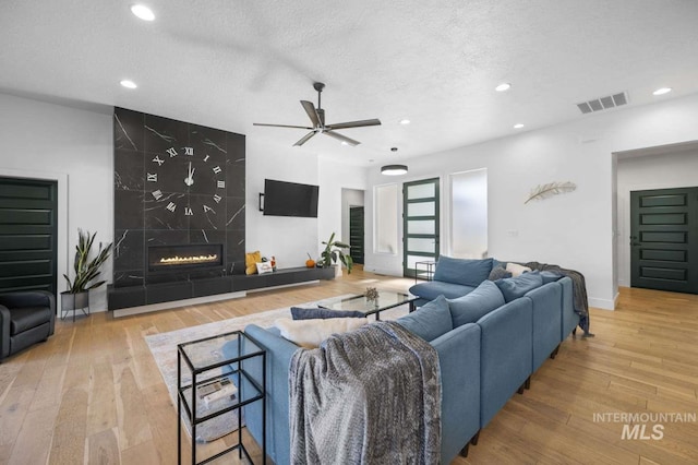 living room featuring ceiling fan, light wood-type flooring, a textured ceiling, and a tiled fireplace