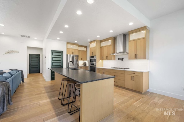 kitchen featuring stainless steel appliances, a spacious island, wall chimney range hood, and light hardwood / wood-style floors