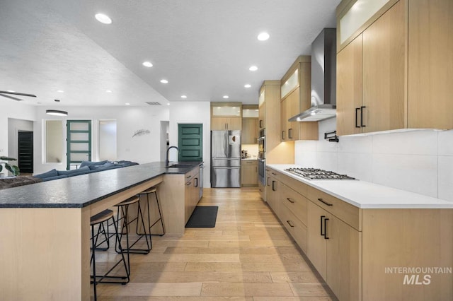 kitchen featuring a large island with sink, light hardwood / wood-style flooring, wall chimney exhaust hood, a textured ceiling, and stainless steel appliances