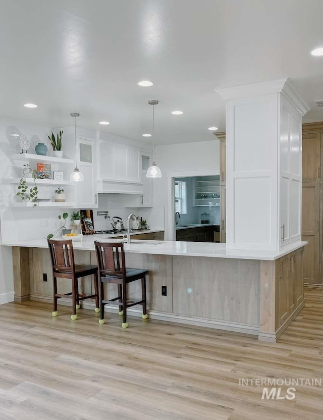 kitchen featuring hanging light fixtures, kitchen peninsula, a breakfast bar, white cabinets, and light wood-type flooring