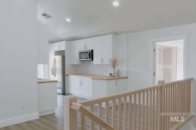 kitchen featuring white cabinets, appliances with stainless steel finishes, light wood-type flooring, and tasteful backsplash