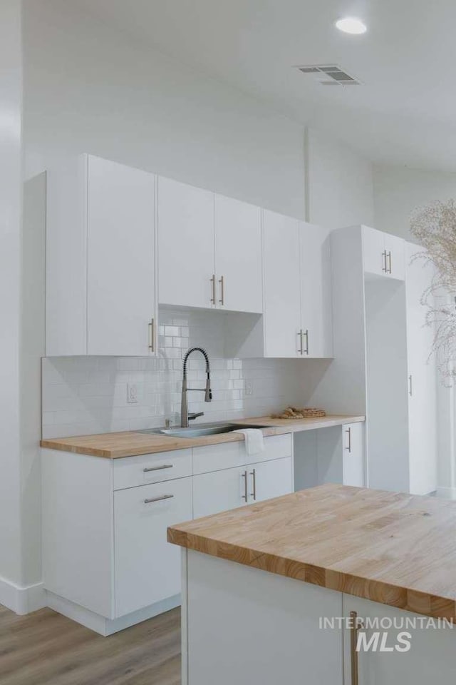 kitchen featuring butcher block countertops, white cabinetry, sink, and light hardwood / wood-style floors