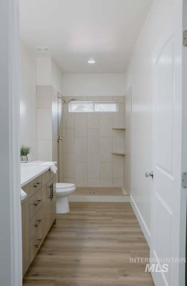 bathroom featuring hardwood / wood-style floors, vanity, toilet, and a tile shower