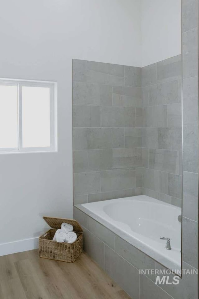 bathroom with tiled bath and wood-type flooring