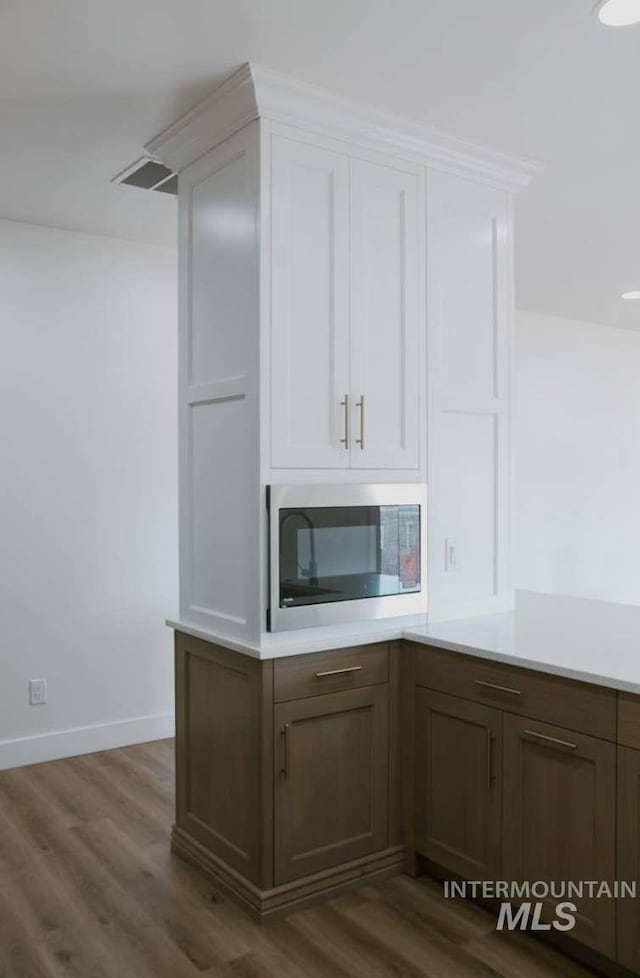 kitchen with white cabinetry, stainless steel microwave, and dark wood-type flooring