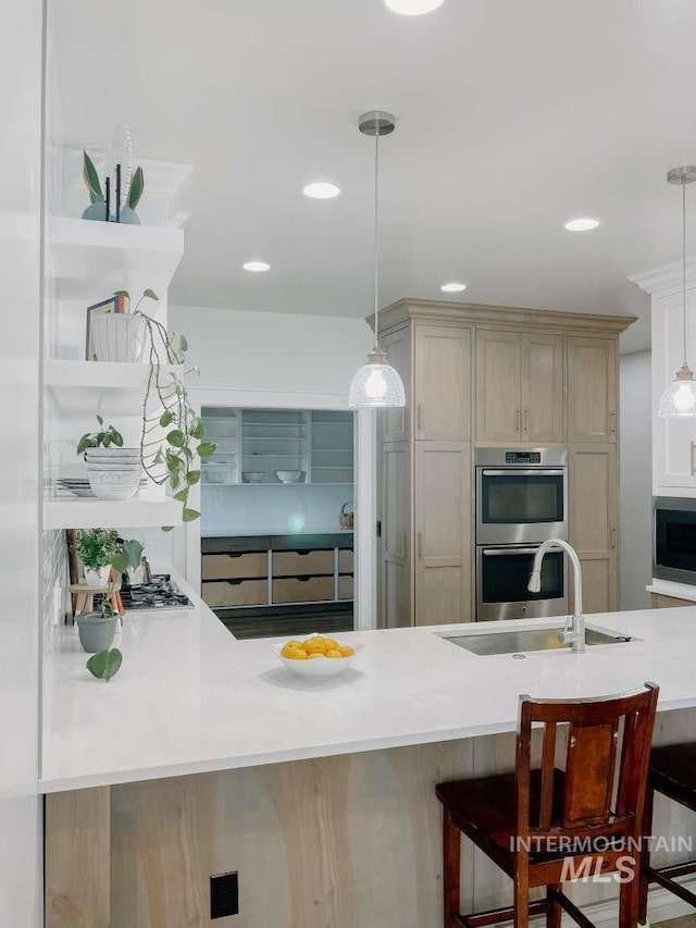 kitchen with light brown cabinetry, a breakfast bar, pendant lighting, and appliances with stainless steel finishes