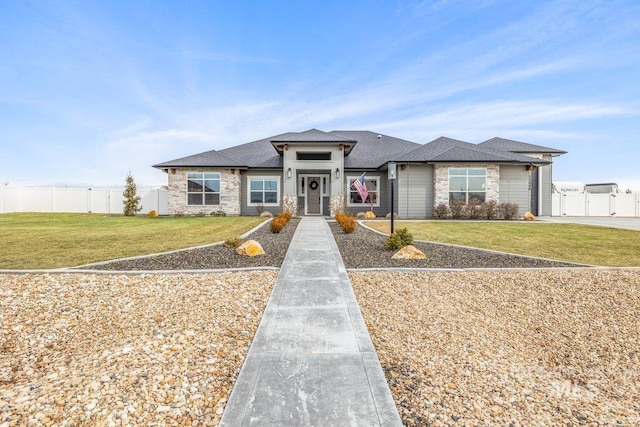 prairie-style home featuring a front lawn, fence, stone siding, and roof with shingles