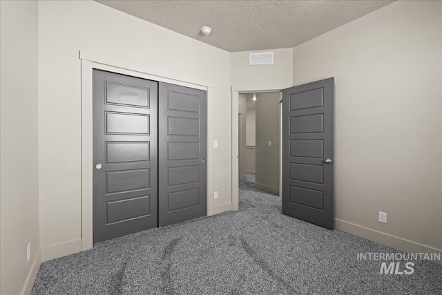 unfurnished bedroom featuring a textured ceiling, visible vents, baseboards, a closet, and dark carpet