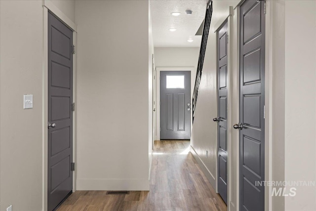 foyer featuring a textured ceiling, wood finished floors, visible vents, and baseboards