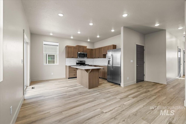 kitchen featuring light countertops, appliances with stainless steel finishes, light wood-type flooring, a center island, and a kitchen bar