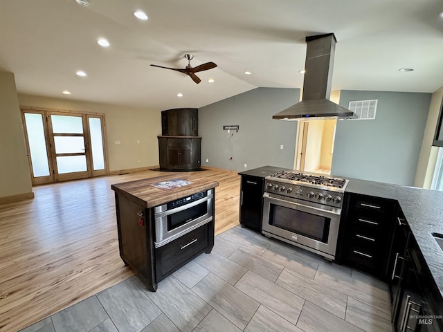 kitchen featuring ceiling fan, dark cabinets, stainless steel appliances, island exhaust hood, and visible vents