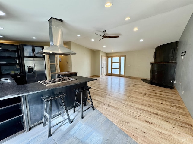 kitchen with ceiling fan, island exhaust hood, light wood-type flooring, a breakfast bar, and stainless steel appliances