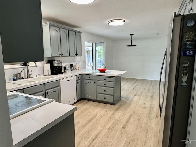kitchen with white dishwasher, a sink, freestanding refrigerator, a peninsula, and gray cabinetry
