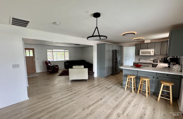 kitchen with visible vents, light countertops, a peninsula, white appliances, and light wood-style flooring