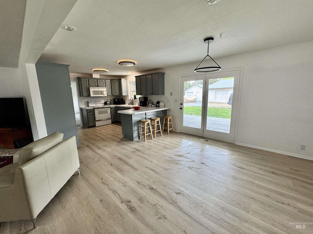 kitchen featuring a peninsula, white appliances, open floor plan, a kitchen bar, and light wood-style flooring