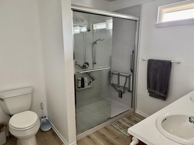 full bath featuring double vanity, a stall shower, wood finished floors, a sink, and toilet