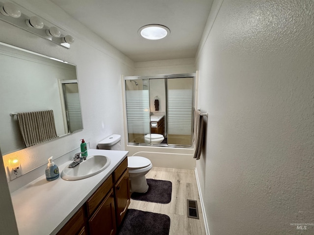 bathroom featuring visible vents, wood finished floors, vanity, toilet, and shower / bath combination with glass door