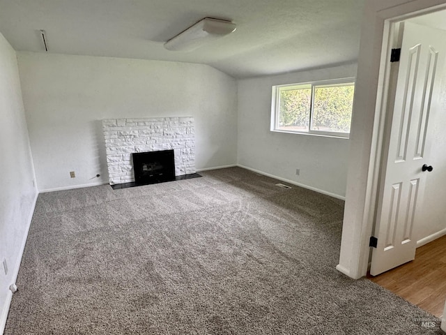 unfurnished living room featuring carpet floors, baseboards, a stone fireplace, and lofted ceiling