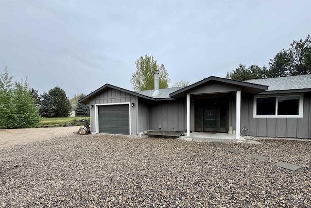 ranch-style house featuring a garage, roof with shingles, board and batten siding, and gravel driveway