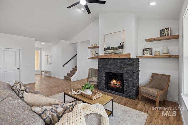 living room with hardwood / wood-style flooring, ceiling fan, a stone fireplace, and vaulted ceiling