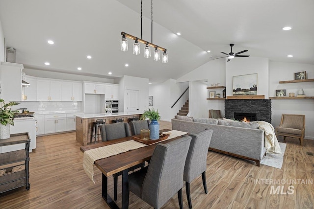 dining room with a stone fireplace, ceiling fan, light hardwood / wood-style flooring, and lofted ceiling