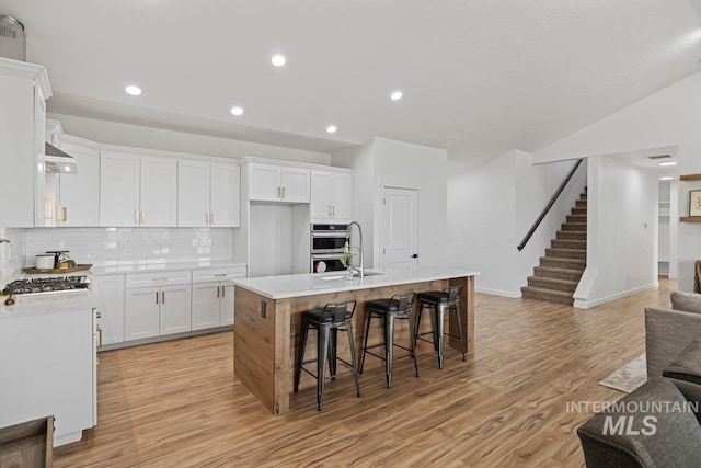 kitchen with tasteful backsplash, sink, light hardwood / wood-style flooring, white cabinets, and an island with sink