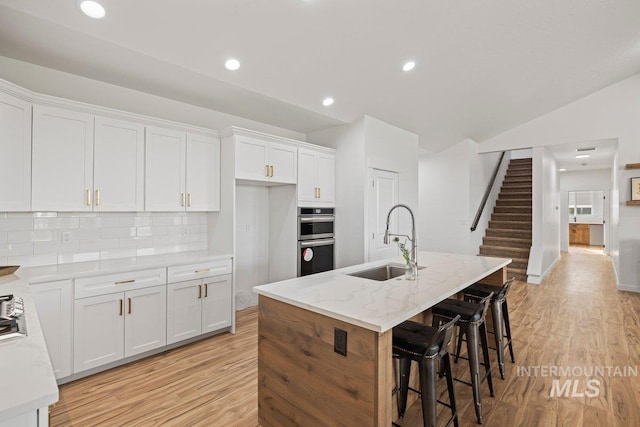 kitchen featuring tasteful backsplash, white cabinets, sink, and an island with sink