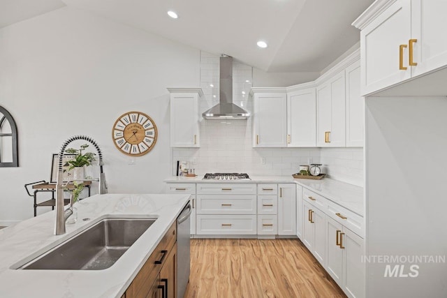 kitchen with appliances with stainless steel finishes, sink, wall chimney range hood, white cabinets, and lofted ceiling