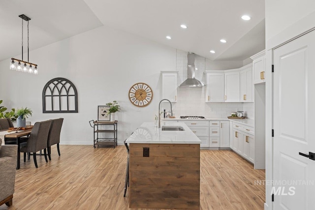 kitchen featuring a kitchen island with sink, wall chimney range hood, sink, light hardwood / wood-style floors, and white cabinetry