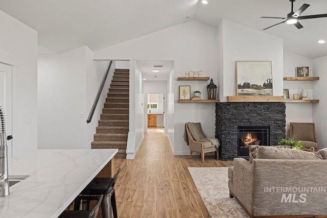 living room featuring a stone fireplace, ceiling fan, light hardwood / wood-style flooring, and lofted ceiling