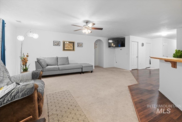 living room with a textured ceiling, dark wood-type flooring, and ceiling fan